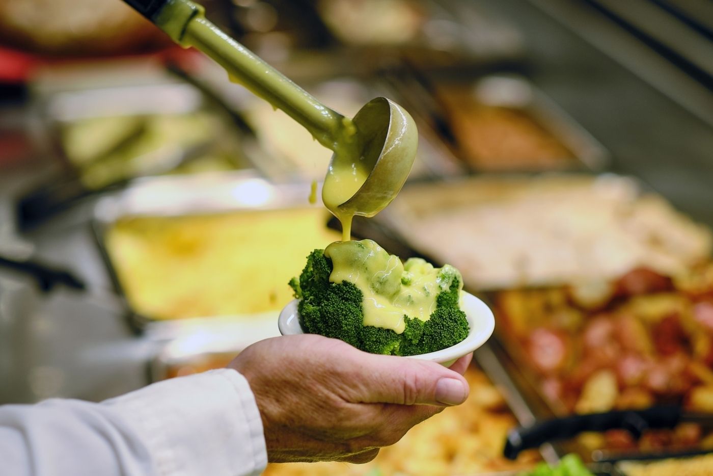 Guest receiving broccoli with cheese sauce on the serving line