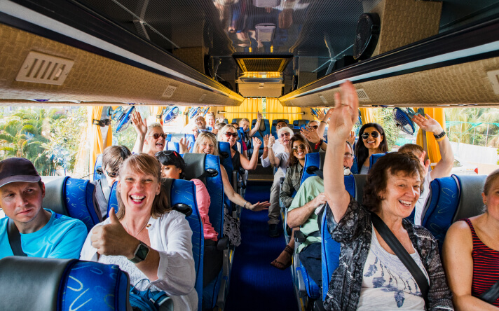 Group on bus smiling with hands in the air